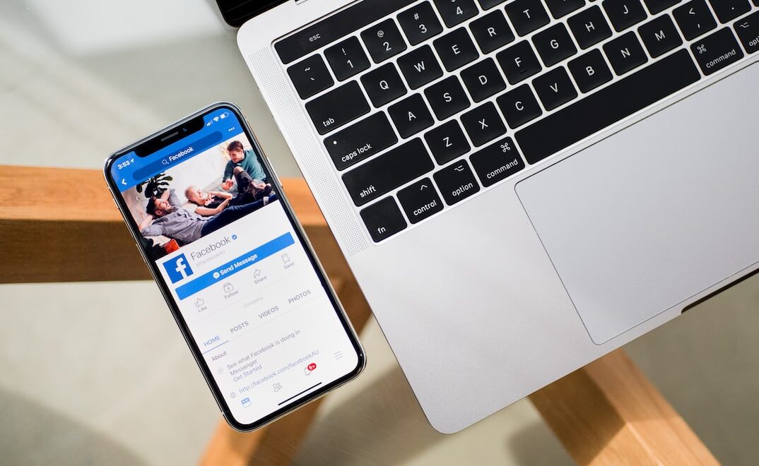Facebook displayed on an iPhone beside a laptop
