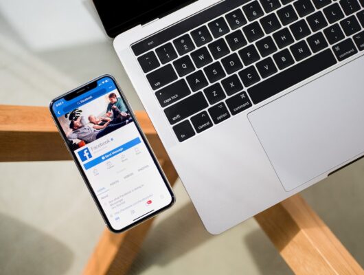 Facebook displayed on an iPhone beside a laptop